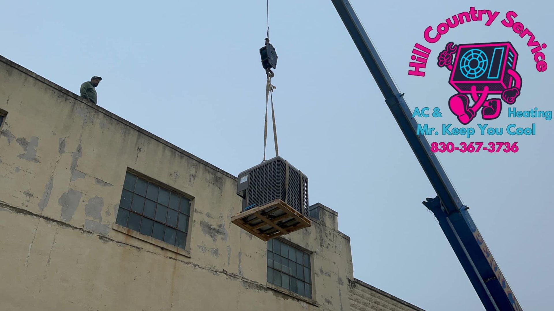 A crane is lifting an air conditioner from the roof of a building