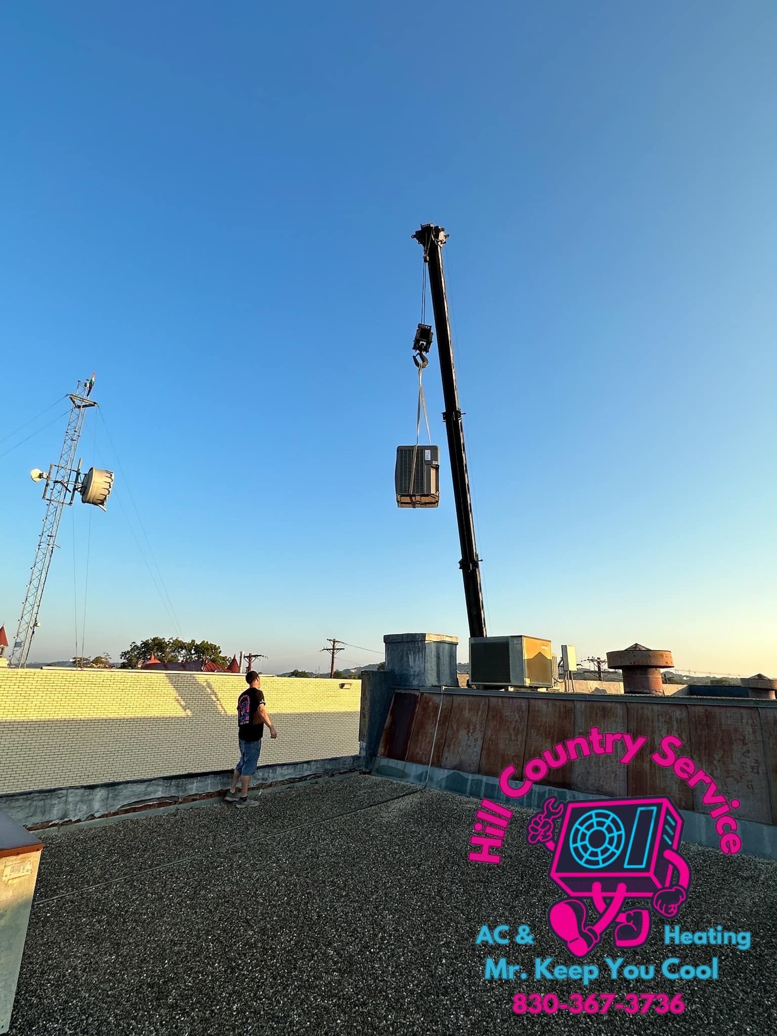 A crane is lifting a machine on top of a roof.