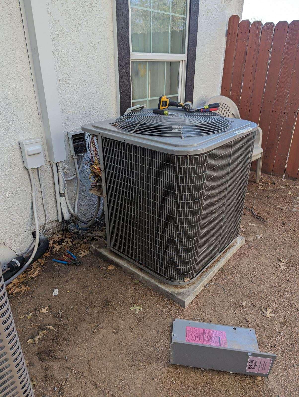An air conditioner is sitting outside of a house next to a window.