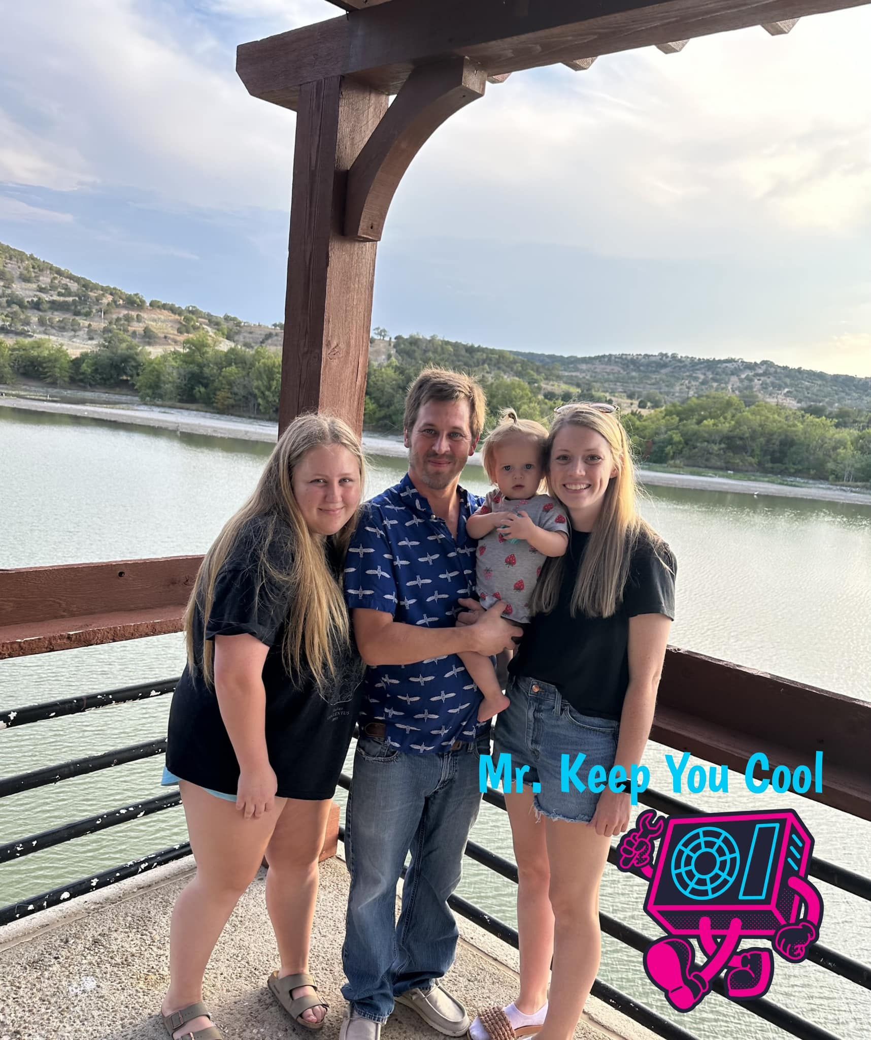 A family is posing for a picture on a balcony overlooking a lake.