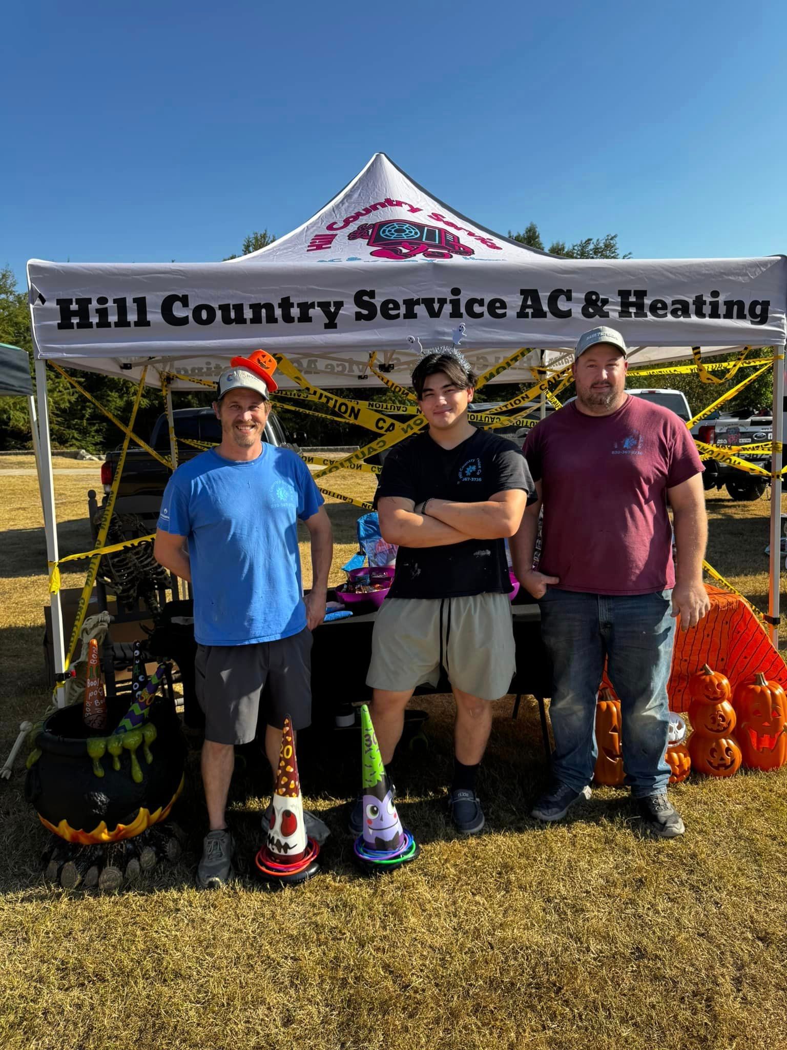 Three men are standing under a tent that says hill country service ac & heating.