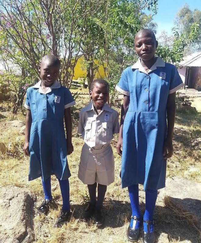 Three children in blue dresses are posing for a picture