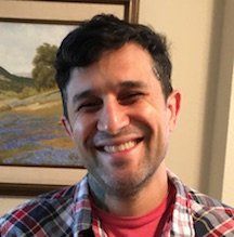 A man in a plaid shirt is smiling in front of a painting.