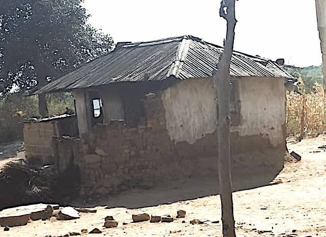 A small house with a tin roof is in the middle of a dirt field.