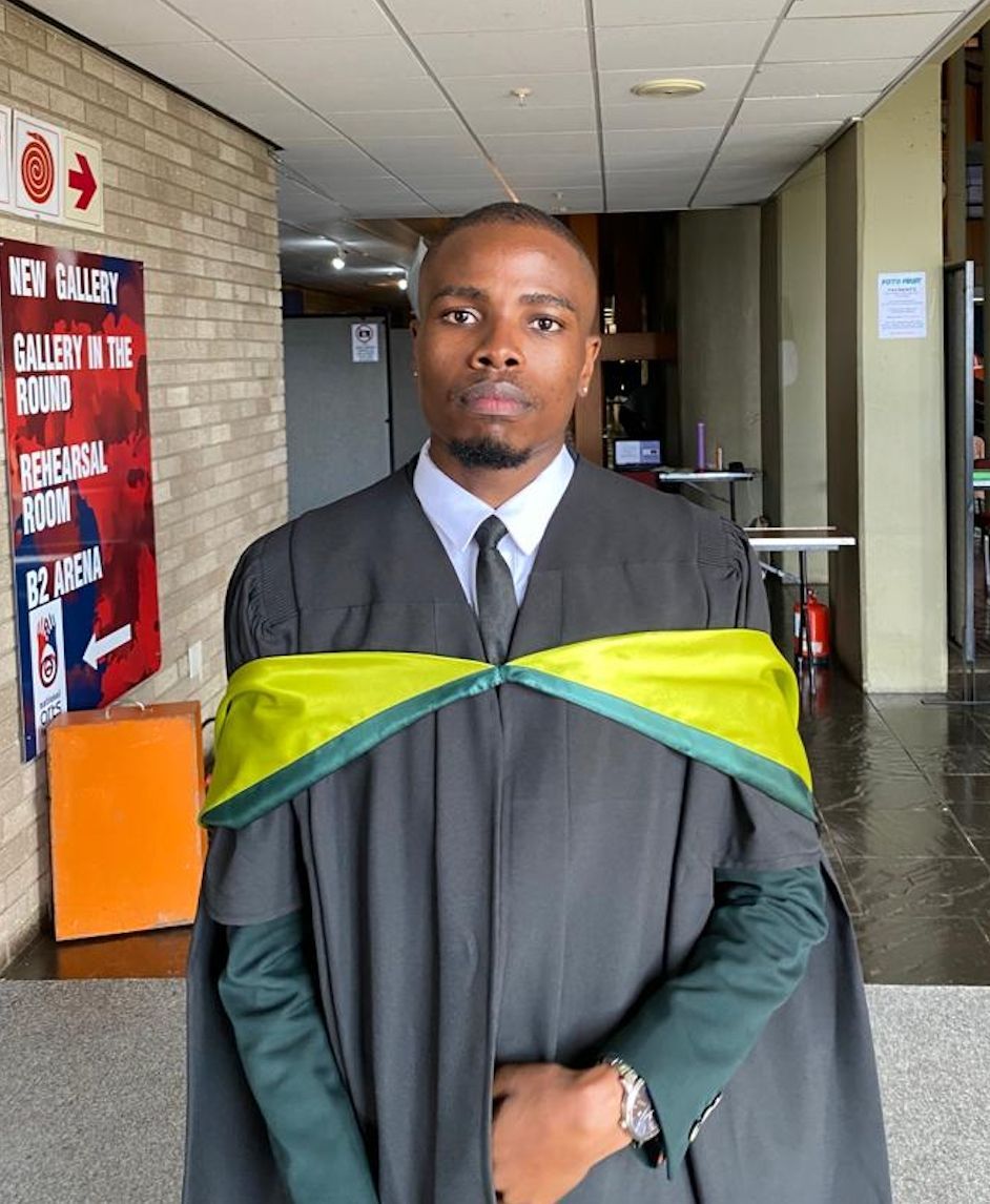 A man in a graduation gown is standing in front of a sign that says new gallery