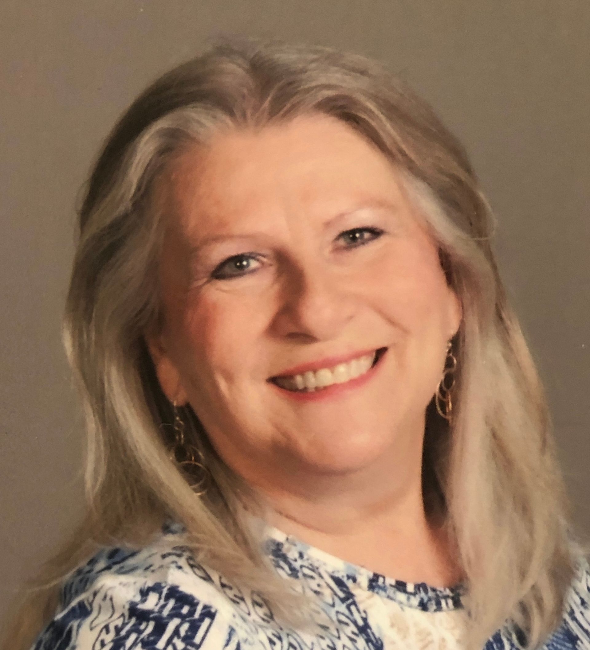 A woman with gray hair is smiling and wearing a blue and white shirt