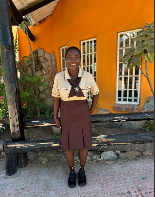 A woman in a uniform stands in front of an orange building