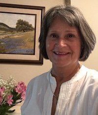 A woman in a white shirt is smiling in front of a painting.