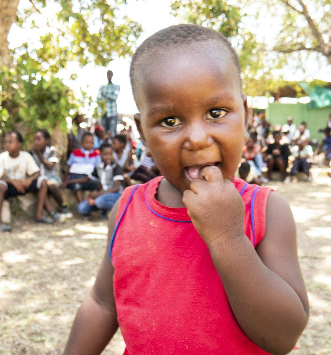 A little boy in a red tank top is looking at the camera