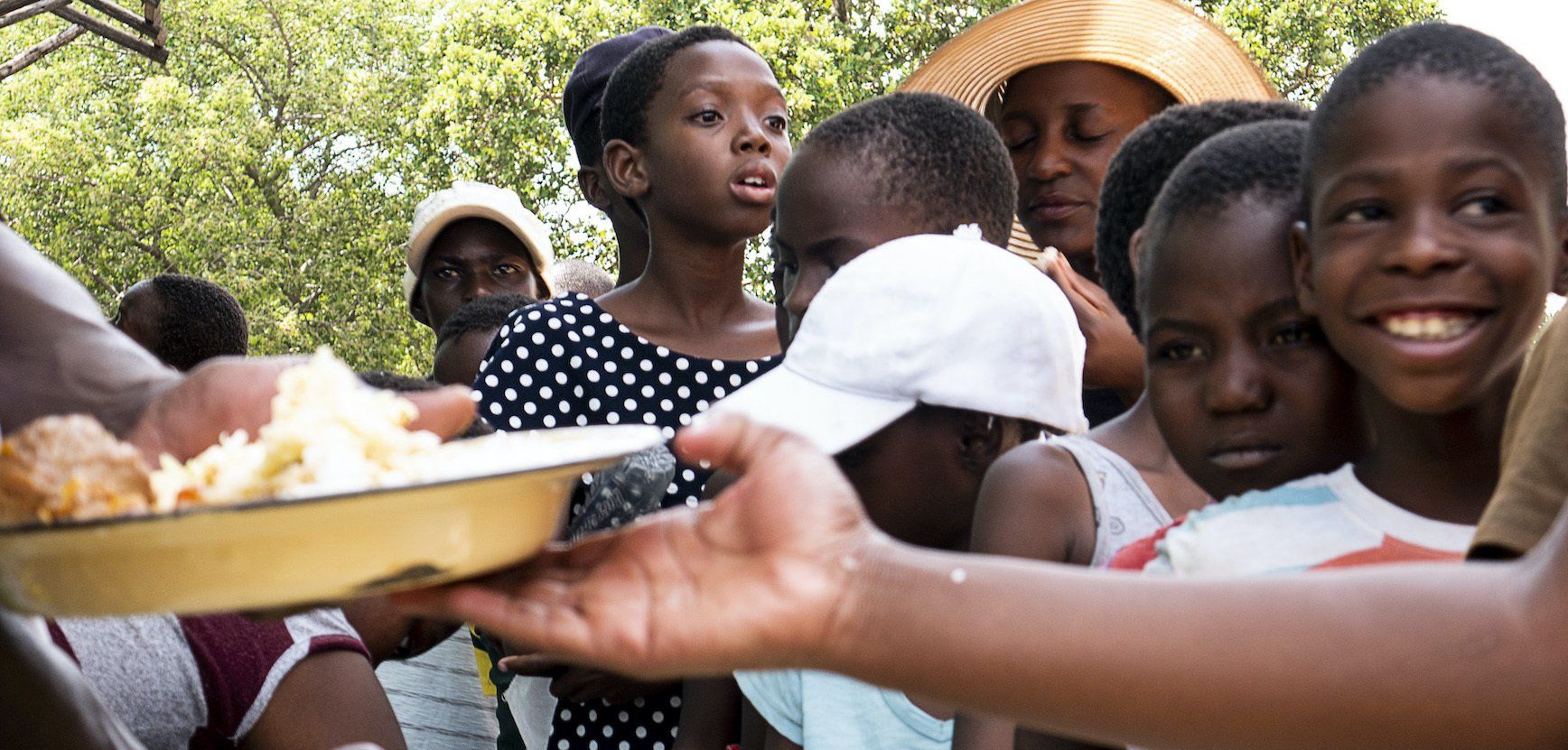 A woman is handing a plate of food to a group of children