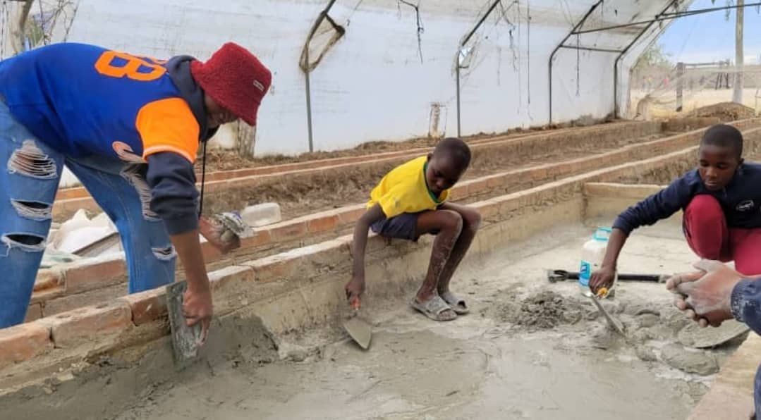 A man and two children are working on a concrete wall.