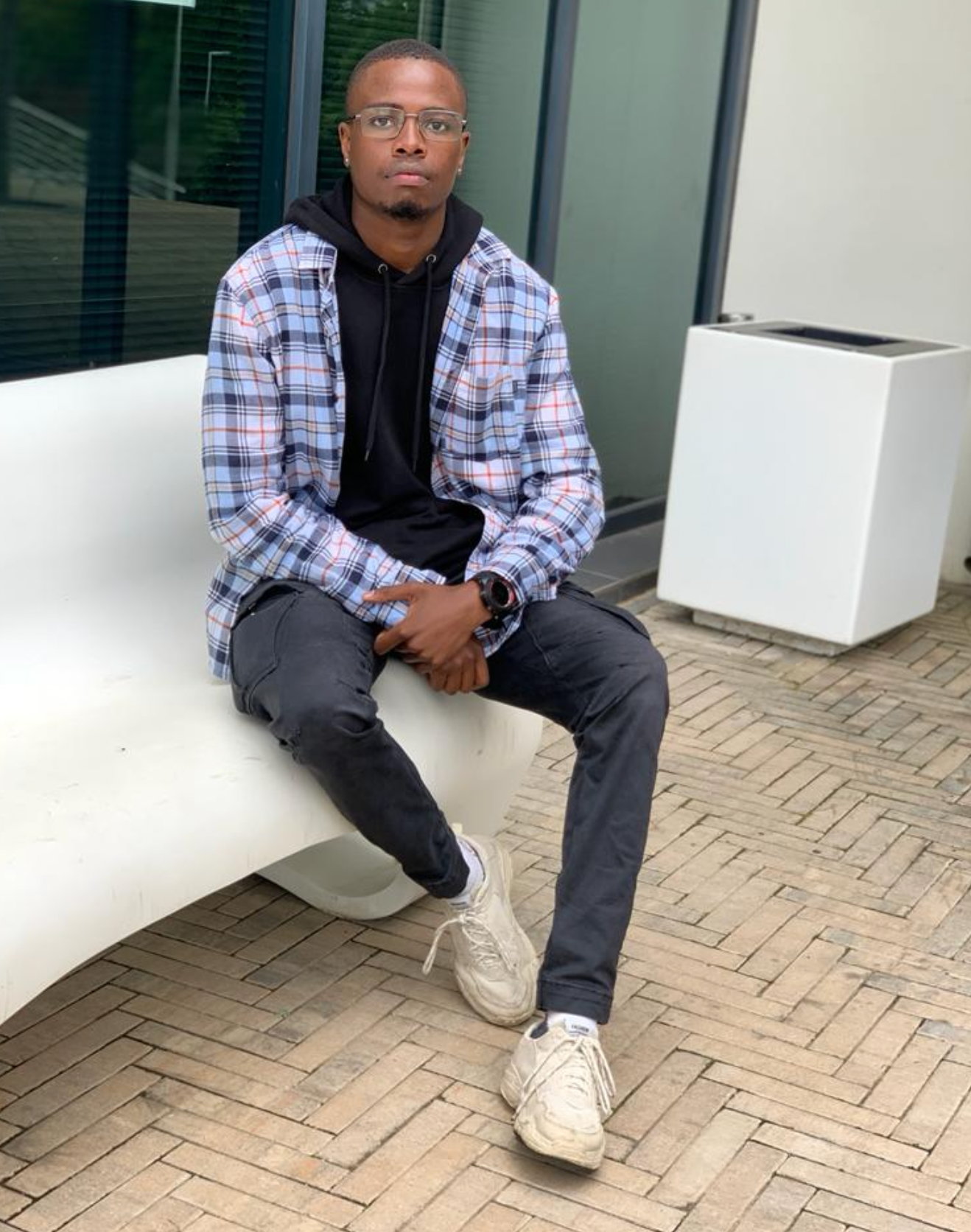 A man is sitting on a white bench on a brick sidewalk.