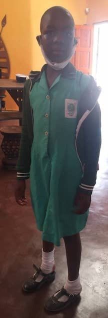 A young boy wearing a green dress and a mask is standing in a room.