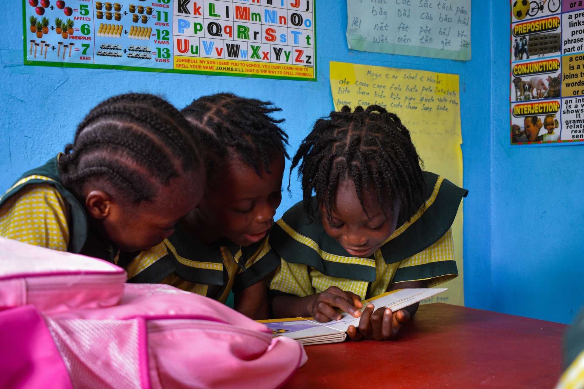 Three children in school uniforms reading a book together at a desk.
