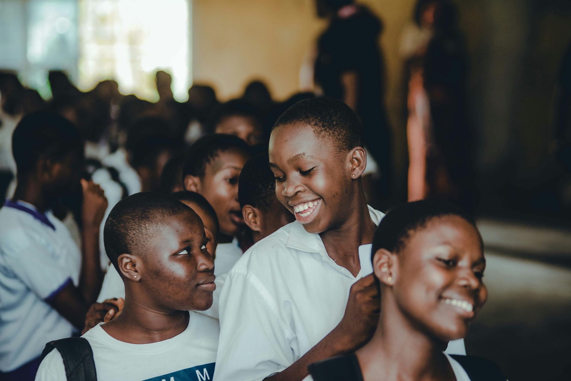 Students in white shirts smile and chat in a brightly lit hallway.