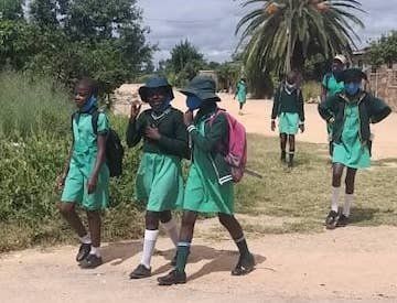 A group of children in green uniforms are walking down a dirt road.