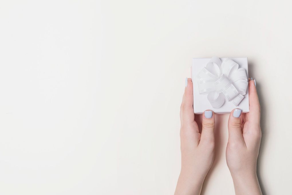 A woman 's hands are holding a white gift box with a bow.
