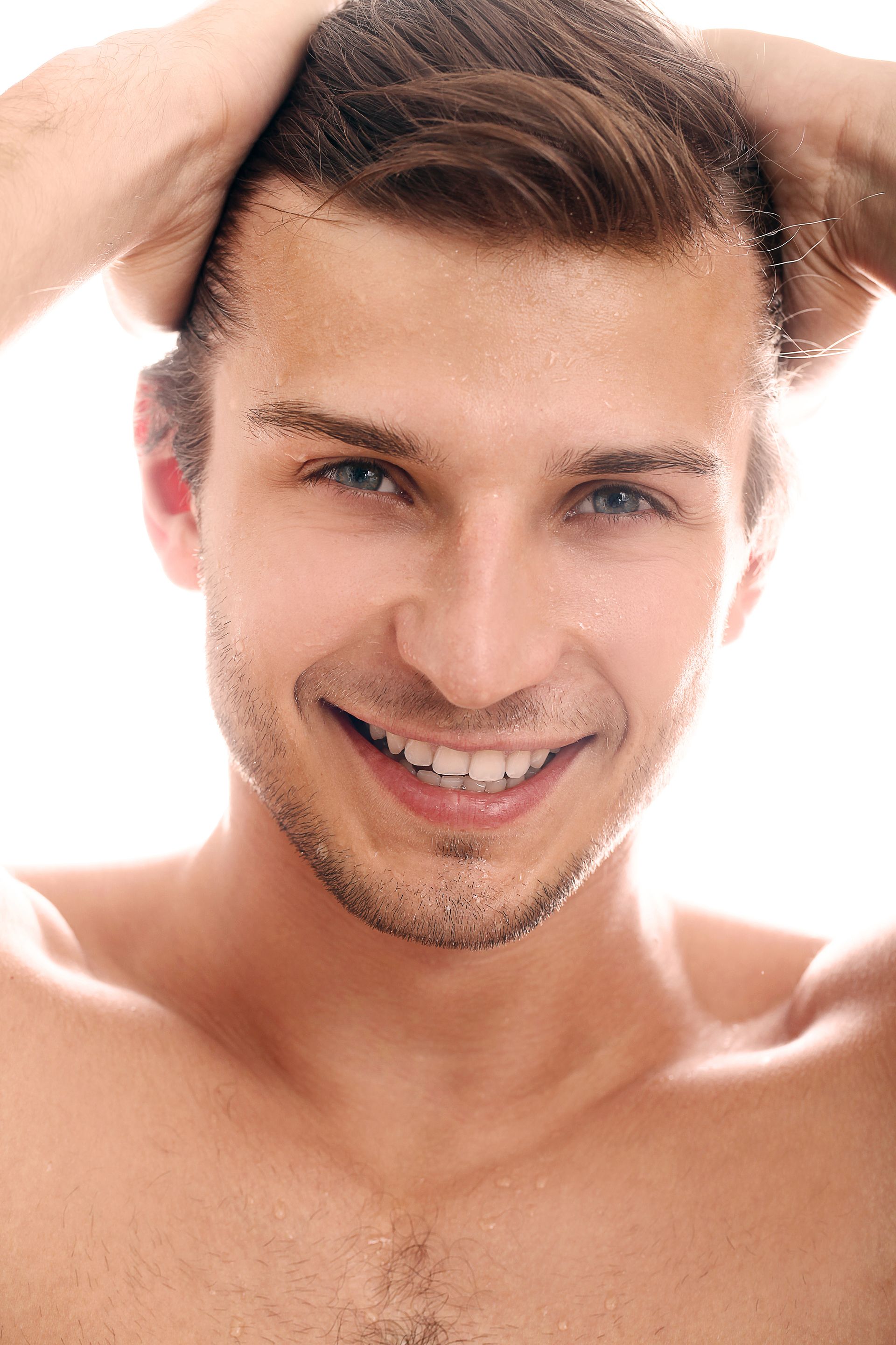 A shirtless man is smiling with his hands in his hair.