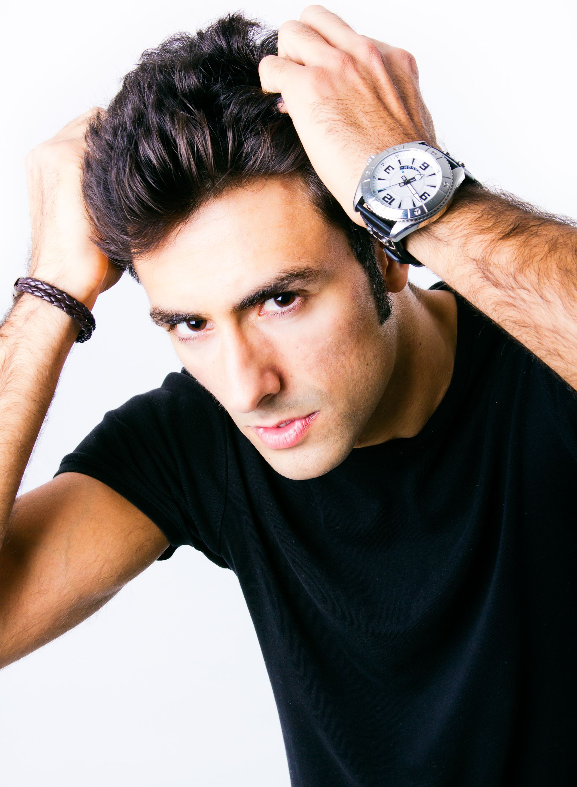 A man wearing a black shirt and a watch adjusts his hair