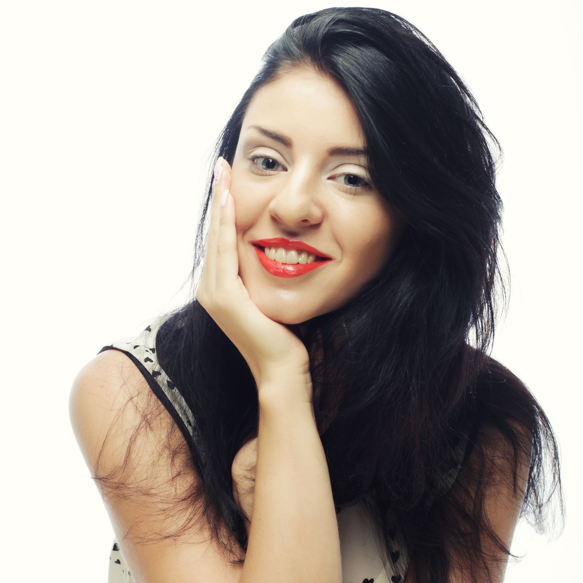 A woman with long black hair is smiling with her hand on her face