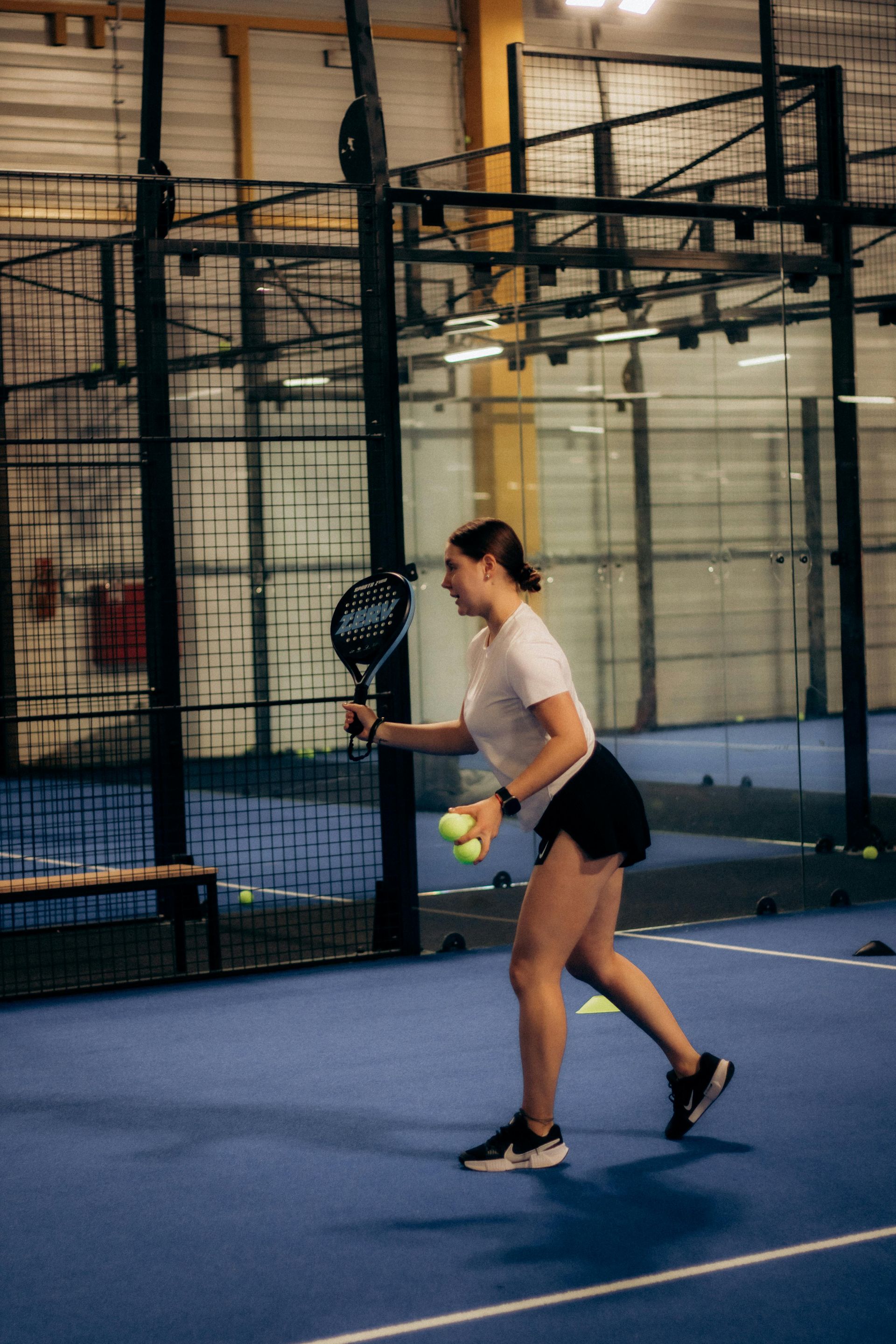 Woman playing tennis on an indoor court, preparing to hit a shot.