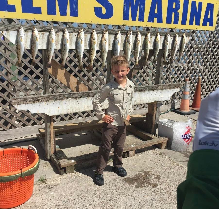A young boy stands in front of a sign that says ' lm 's marina '
