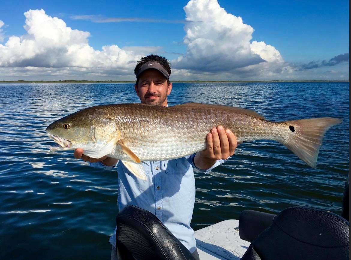 A man is holding a large redfish on a boat in the water.