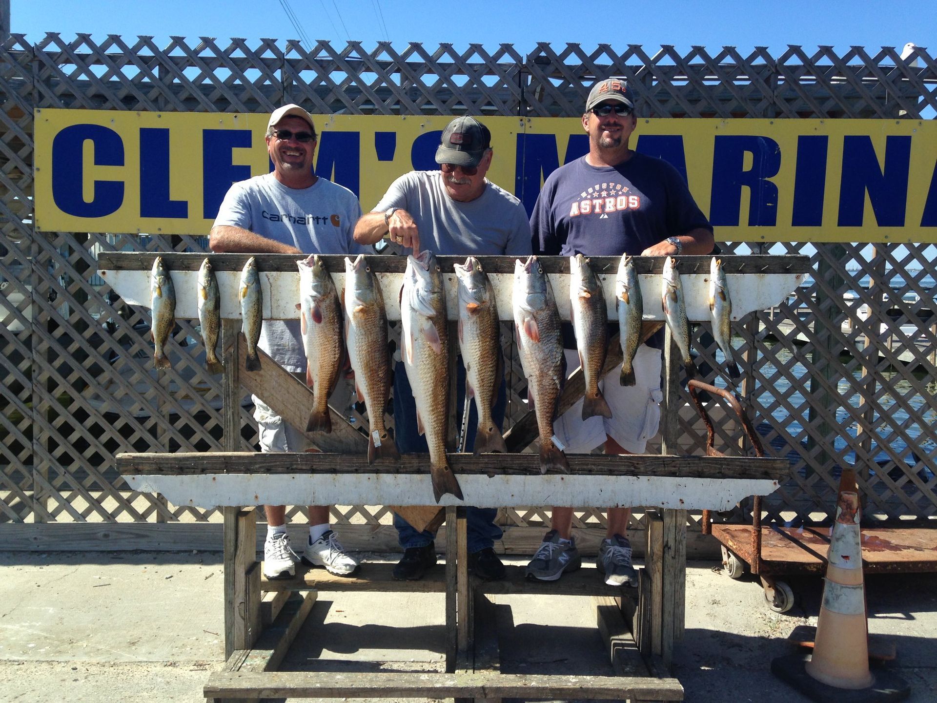 Three men holding fish in front of a sign that says cleveland marina