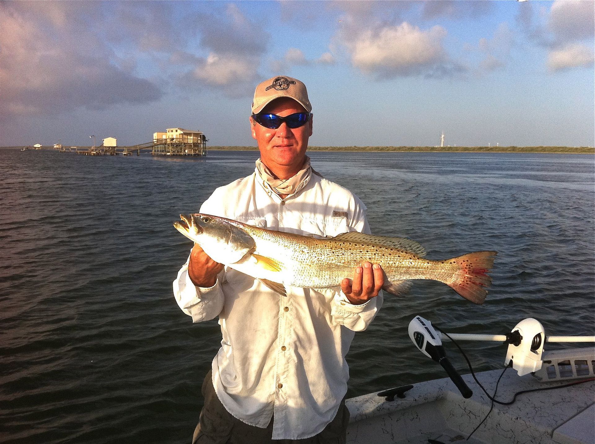 A man is holding a large fish in front of a body of water