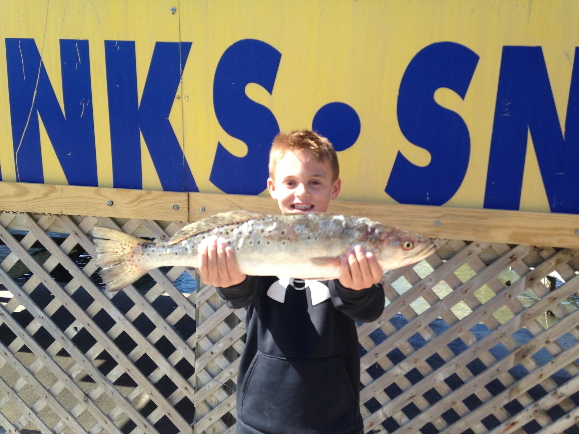 A boy holding a fish in front of a sign that says nks sn
