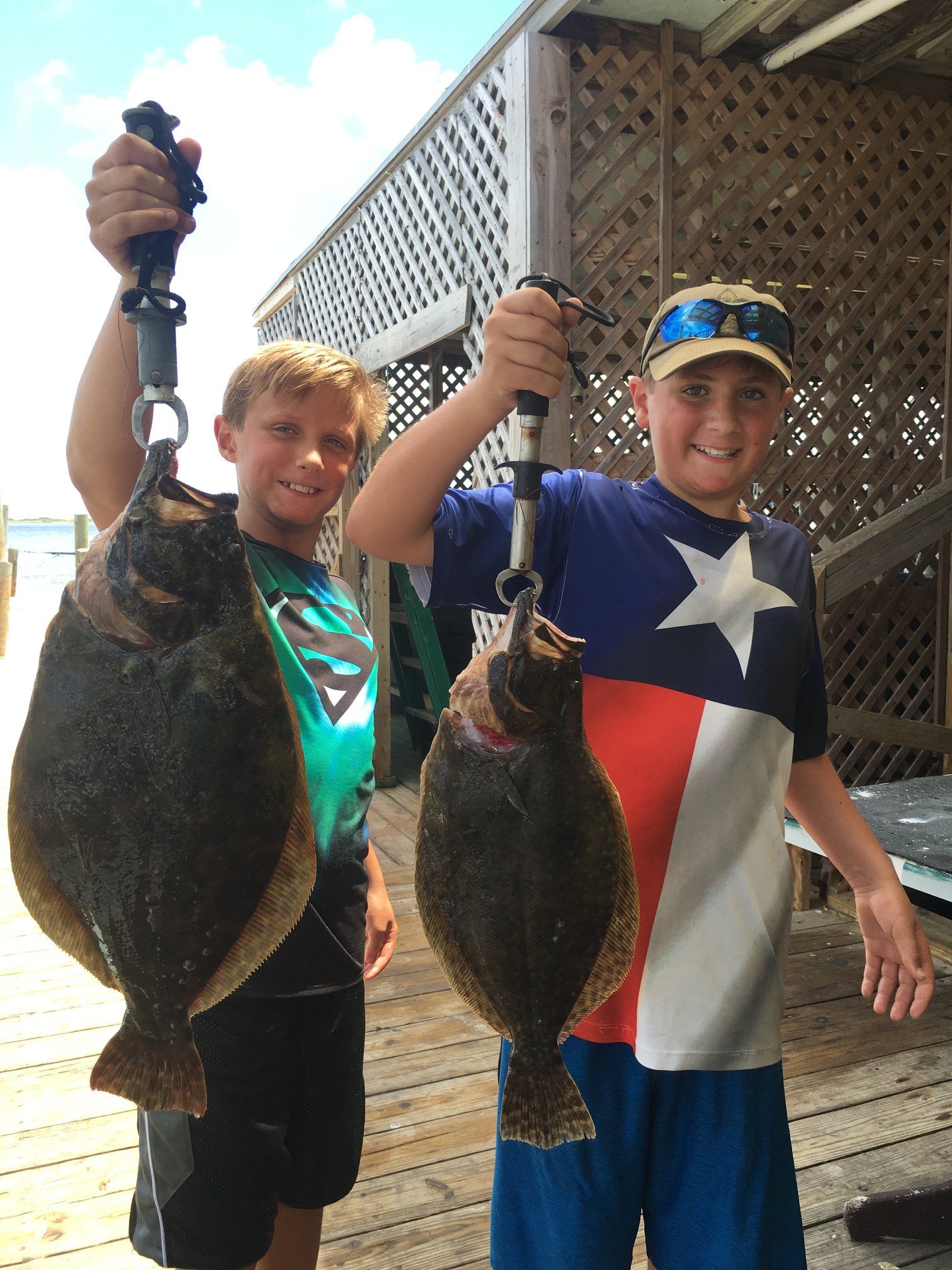 Two young boys are holding two fish in their hands on a deck.