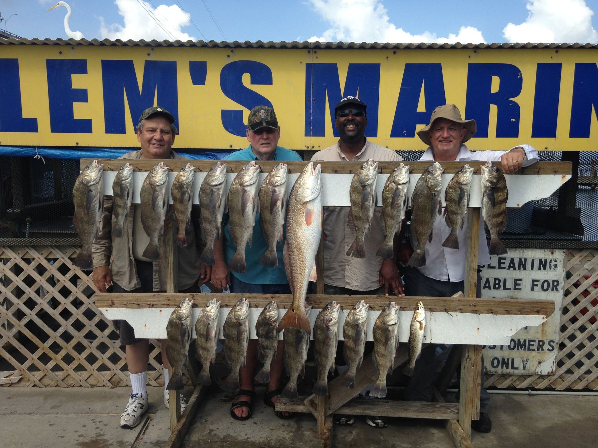 A group of men holding fish in front of a lem 's marina sign
