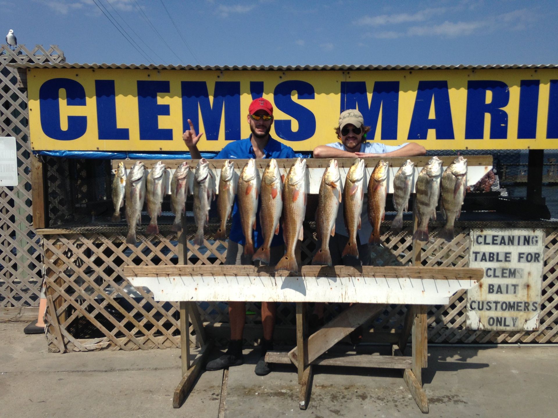 Two men holding fish in front of a sign that says clem 's mari