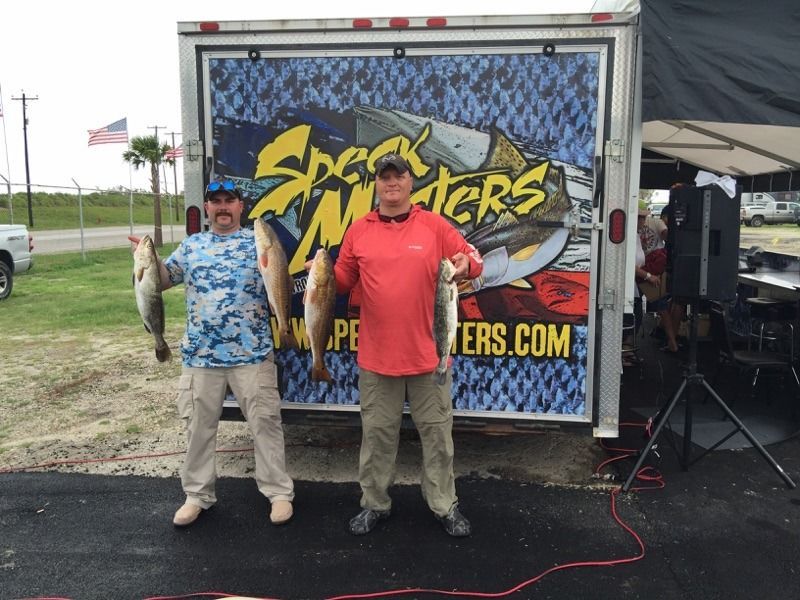 Two men holding fish in front of a trailer that says spec masters