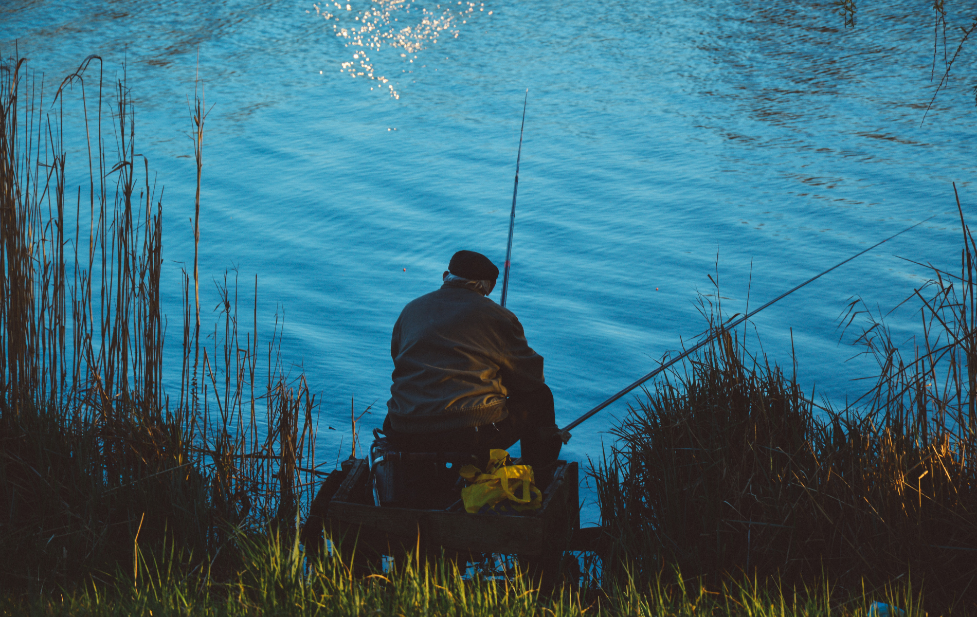 A man is sitting on a dock fishing in a lake.