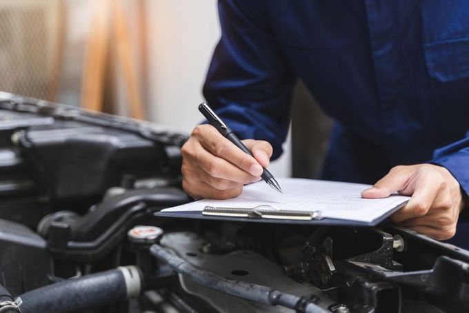 A mechanic is writing on a clipboard while working on a car.