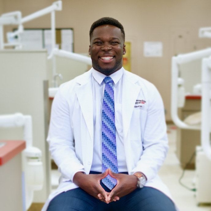 A man in a lab coat and tie is sitting in a dental office