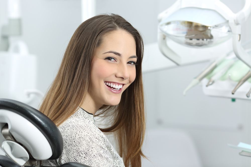 A woman is smiling while sitting in a dental chair.