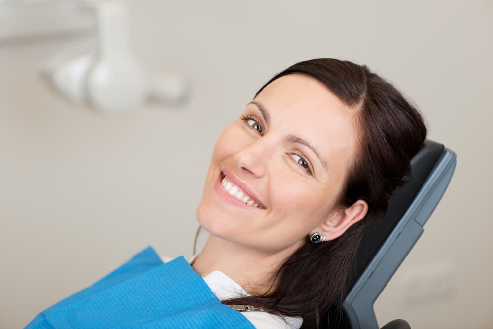 A woman is smiling while sitting in a dental chair.