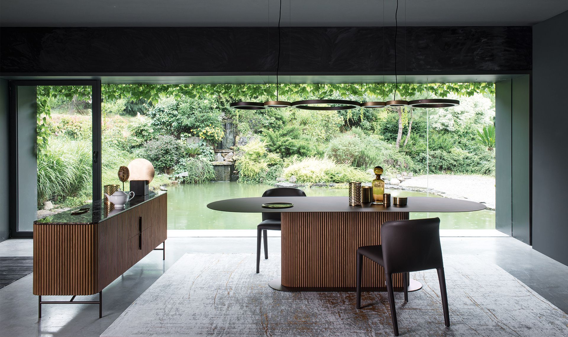 Sala da pranzo con mobili in legno e vista sullo stagno. Tavolo ovale, sedie, credenza e lampade decorative.
