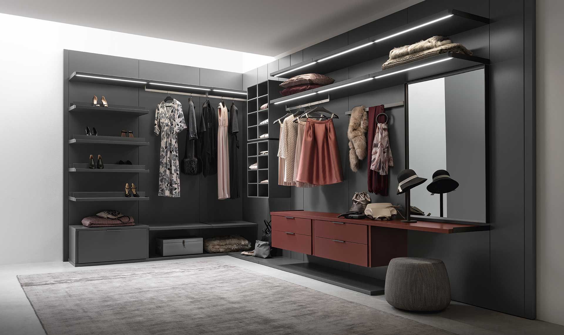 Cabina armadio con pareti grigie, vestiti, scaffali, una toletta con specchio e un tappeto.
