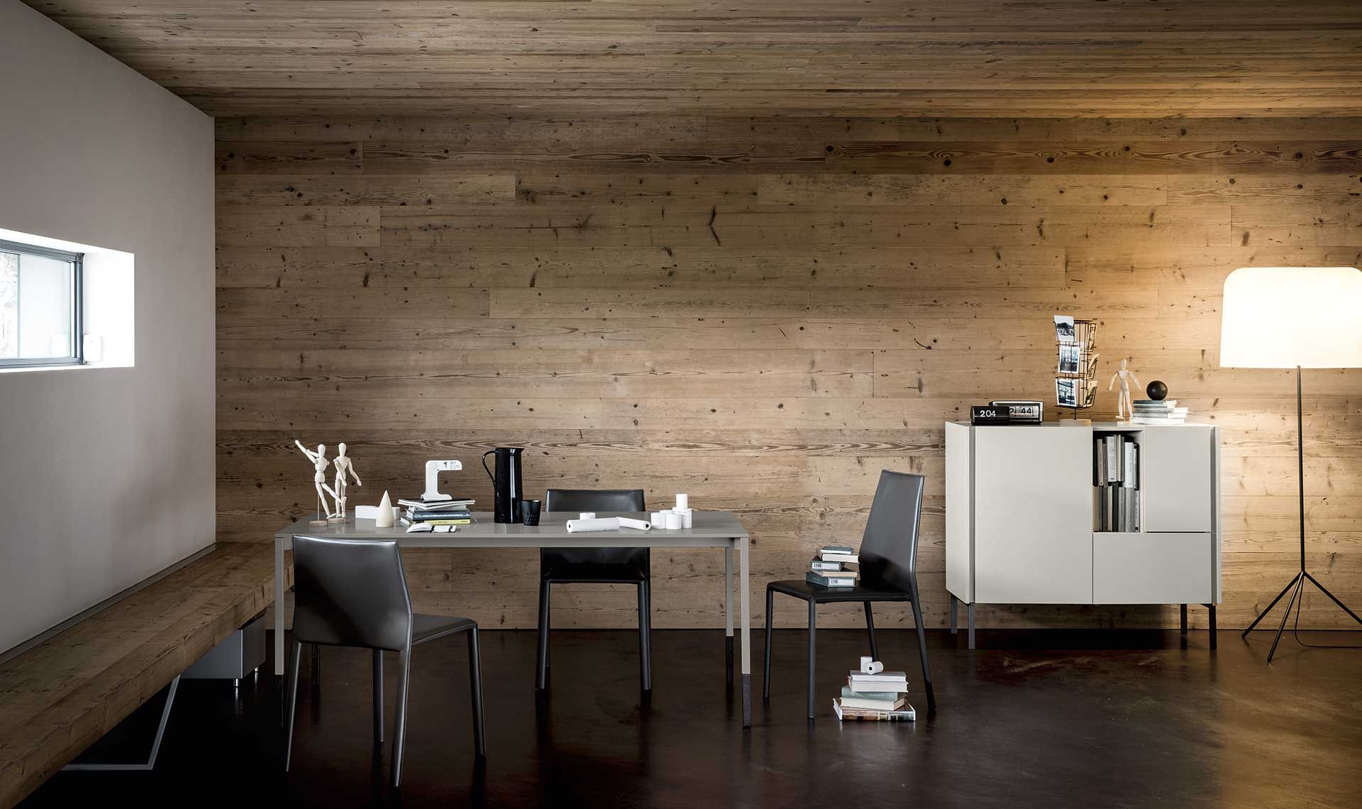 Moderno spazio ufficio con scrivania, sedie, un mobile e una lampada da terra contro una parete rivestita in legno.