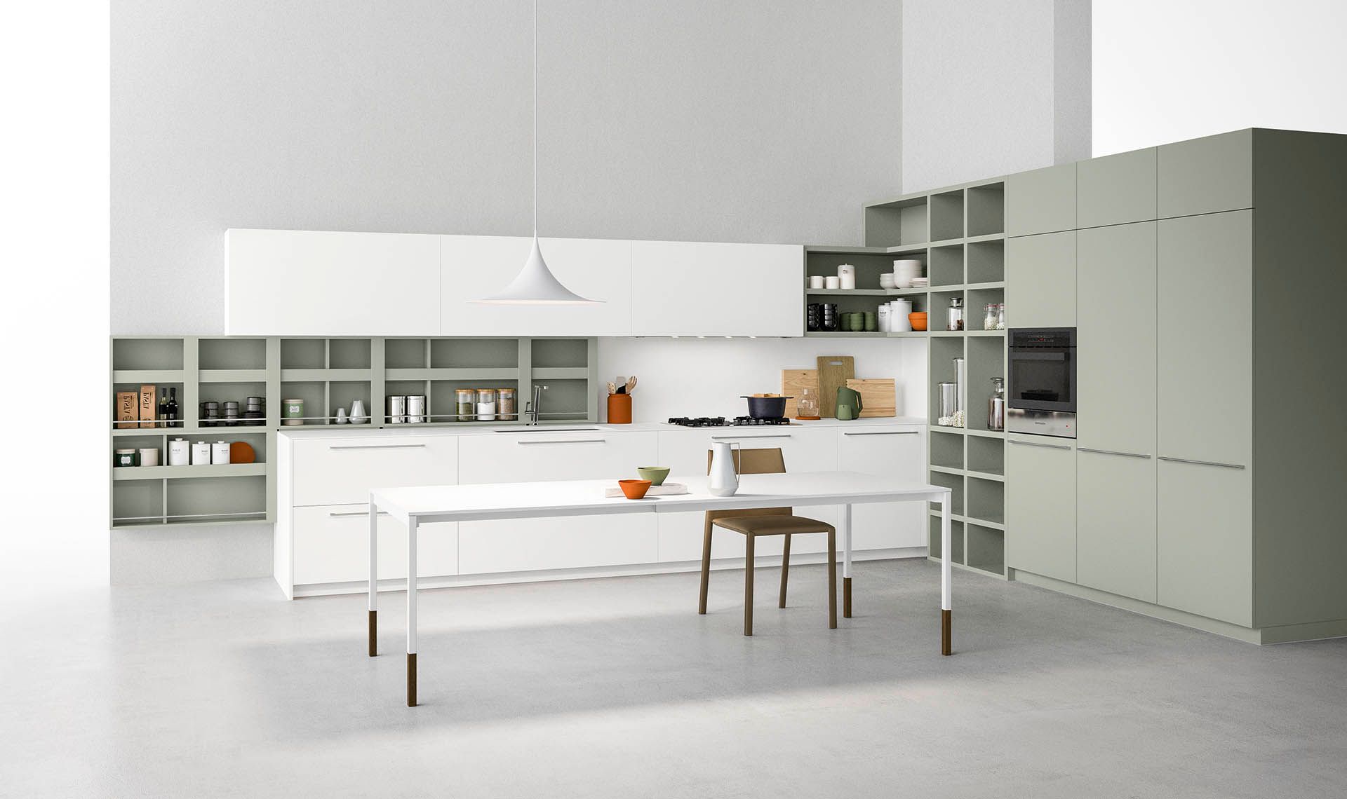 Cucina moderna e minimalista con mobili bianchi e verdi, un lungo tavolo e scaffali aperti.