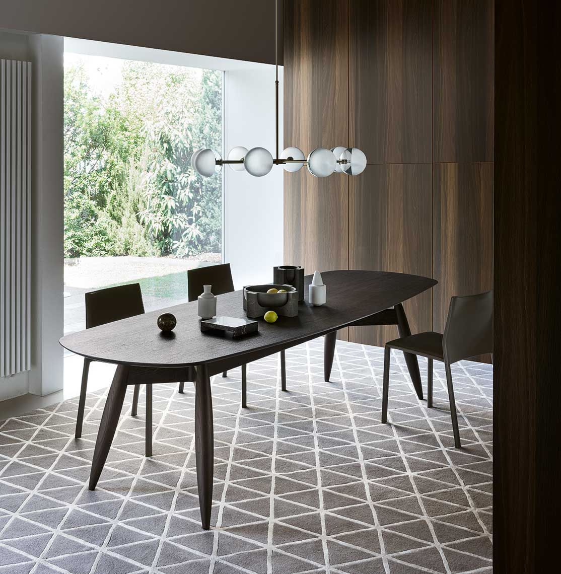 Sala da pranzo con tavolo in legno scuro, sedie e lampada a sospensione; tappeto a fantasia; vista sul giardino.