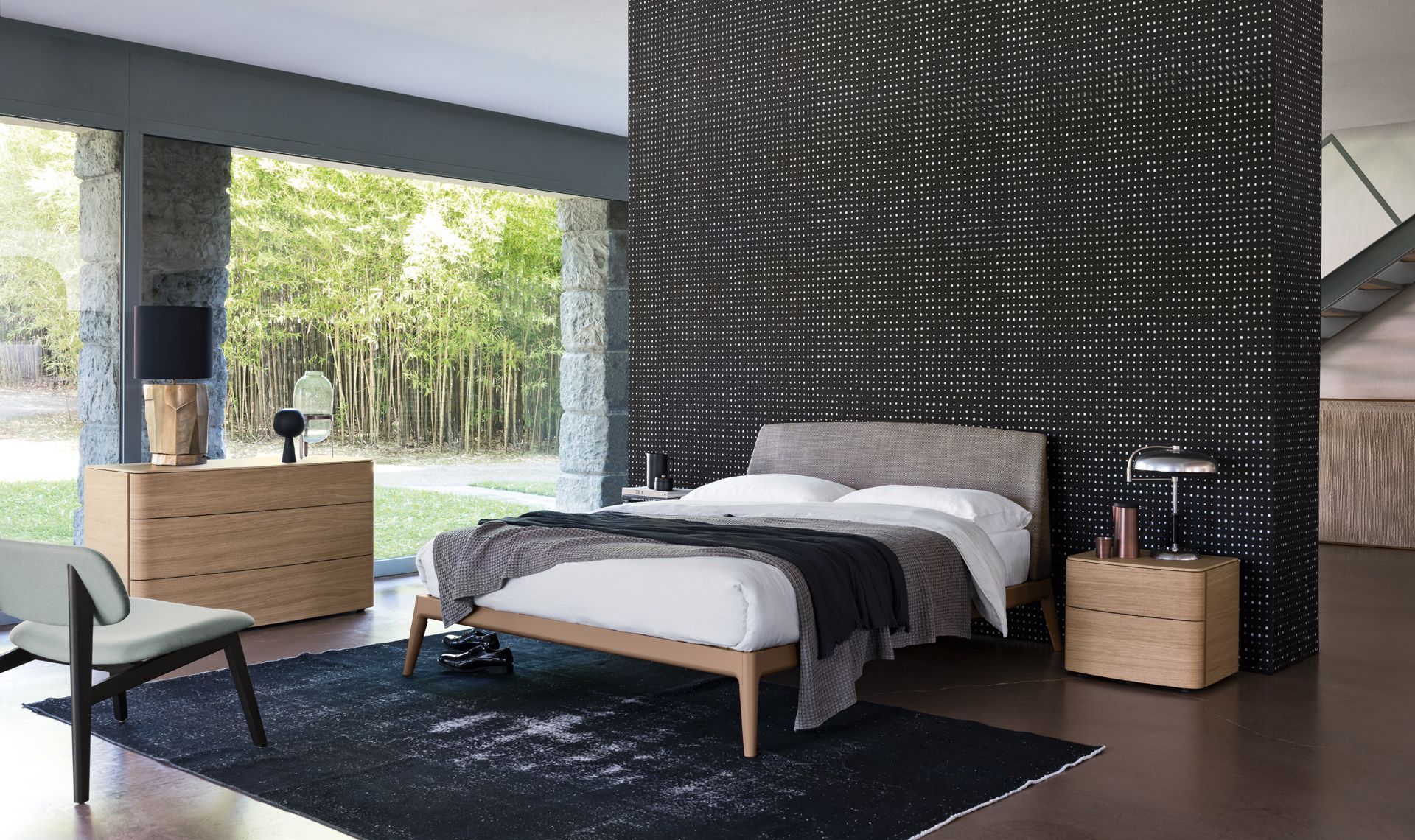 Camera da letto con mobili in legno, ampie finestre e una parete decorativa con texture scura.