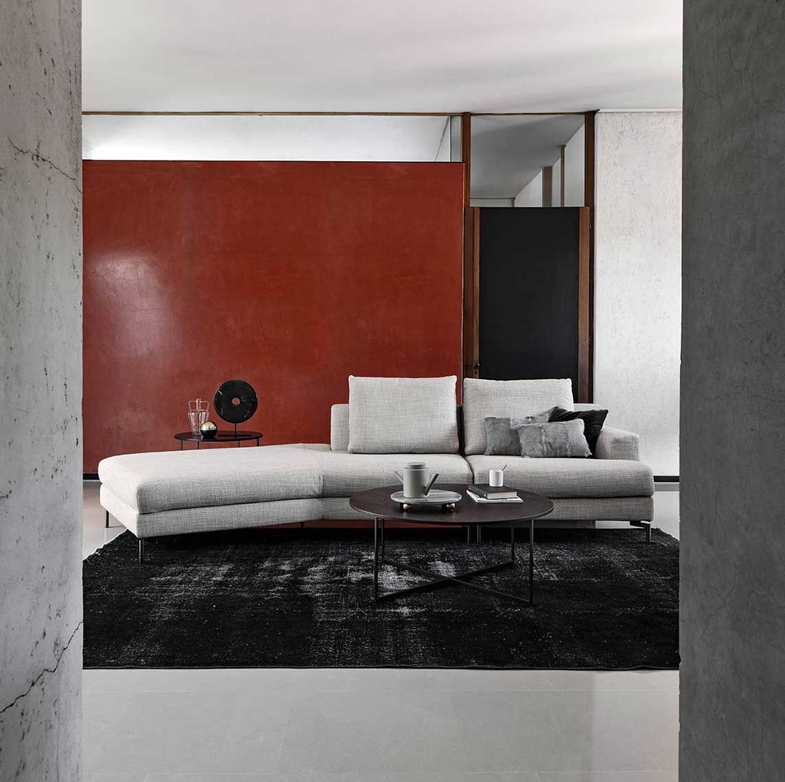 Soggiorno moderno con divano grigio, tappeto nero e parete decorativa rossa.