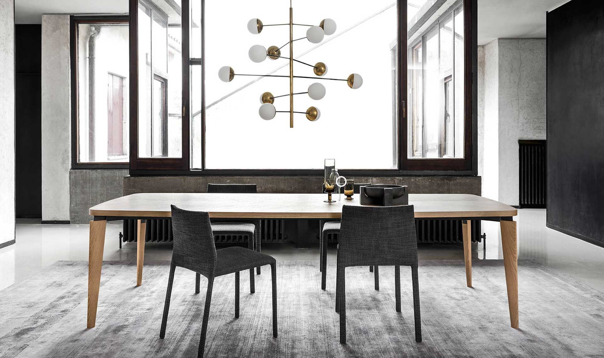 Sala da pranzo con lungo tavolo in legno, sedie nere e lampadario moderno di fronte alle grandi finestre.