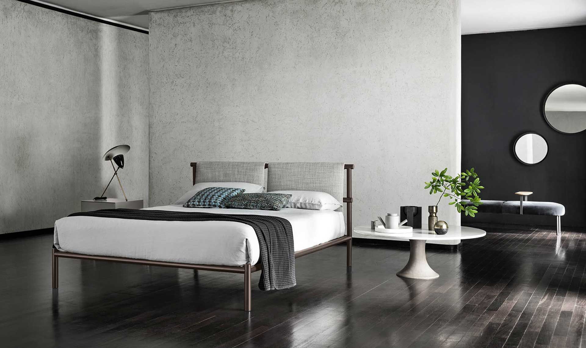 Camera da letto moderna con letto, tavolino, pavimenti scuri e specchi decorativi.