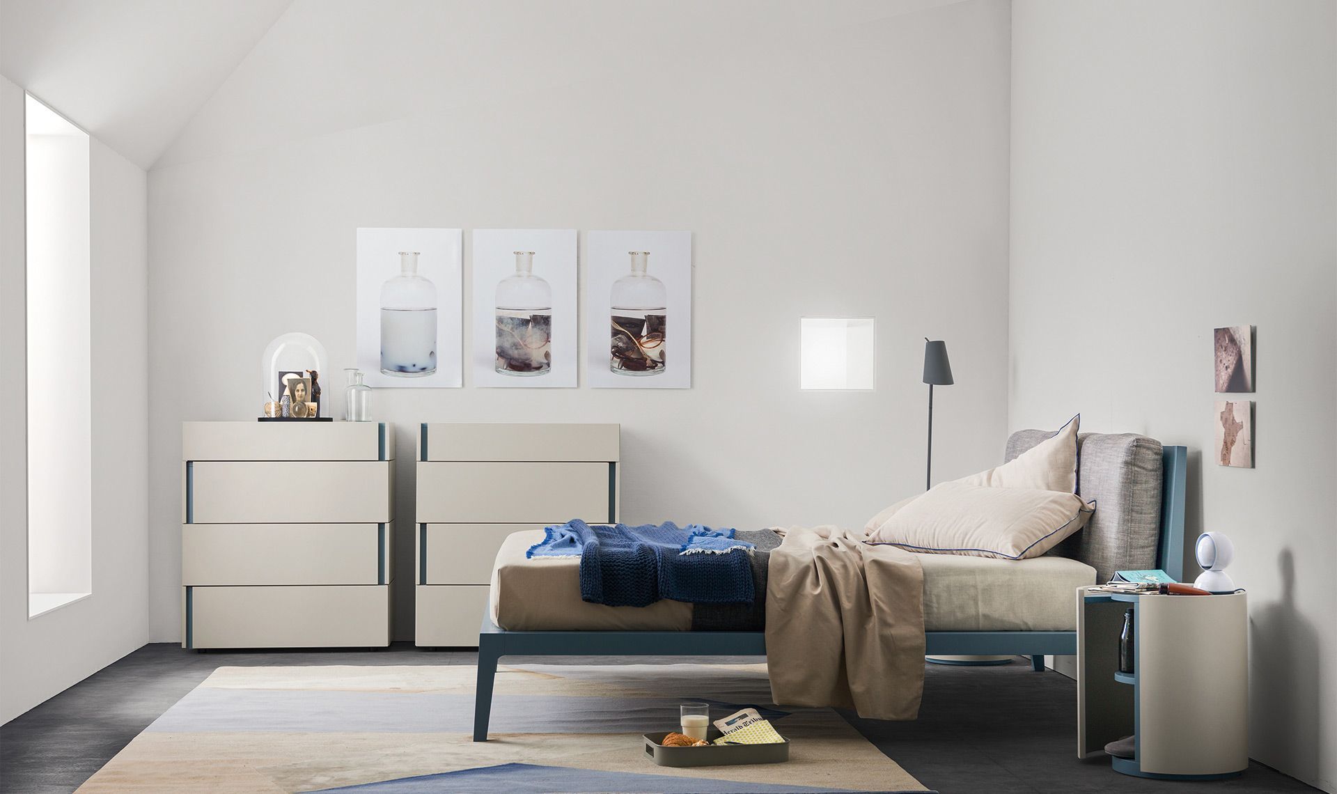 Camera da letto con un letto, due cassettiere, quadri e un comodino. Struttura del letto blu scuro e pareti chiare.