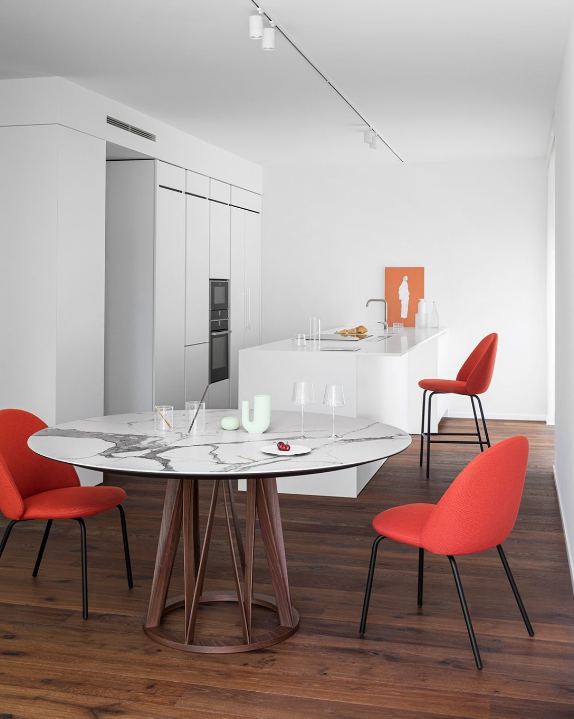 Sala da pranzo moderna: tavolo rotondo in marmo con tre sedie arancioni, cucina bianca sullo sfondo.